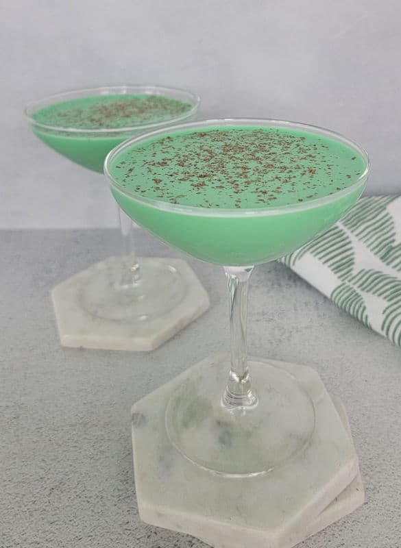 Two green cocktails on white coasters by a green and white cloth napkin