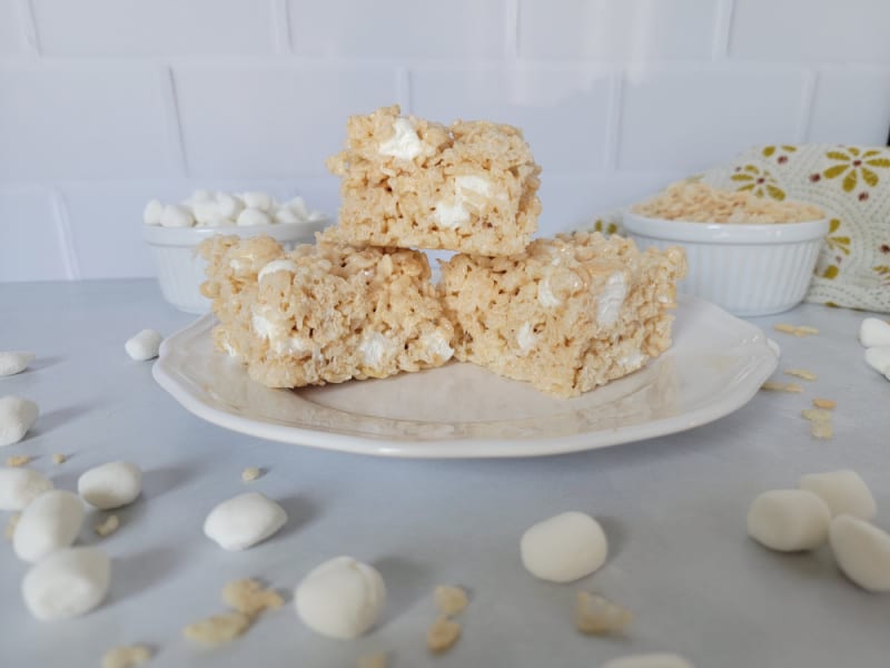 Gooey Rice Krispie Treats stacked on a white plate with mini marshmallows surrounding the plate