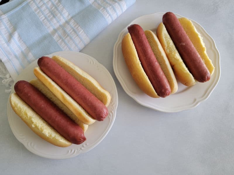 Two plates with 2 hot dogs and buns on a white counter