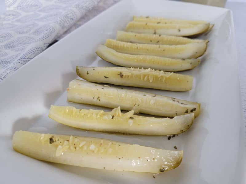 Ranch pickles lined up on a white platter next to a cloth napkin 