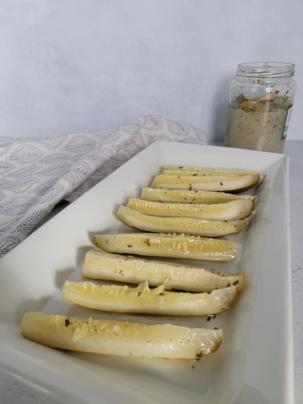 Ranch pickles lined on a white platter next to a cloth napkin and pickle jar. 