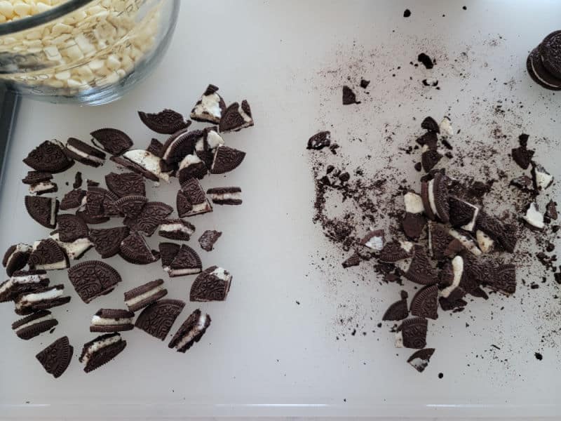 pile of Oreo pieces, a bowl of white chocolate chips on a cutting board. 