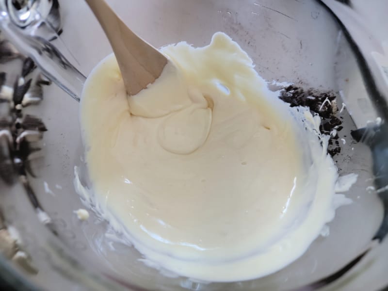 Melted white chocolate in a glass bowl with a wooden spoon