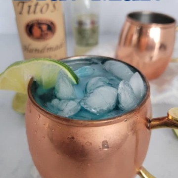 Blue Mule text over a copper mule mug with lime and a bottle of Titos Vodka and Ginger beer