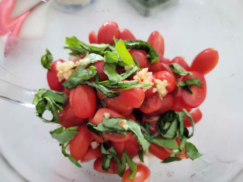 cut cherry tomatoes with garlic and basil strips in a glass bowl 