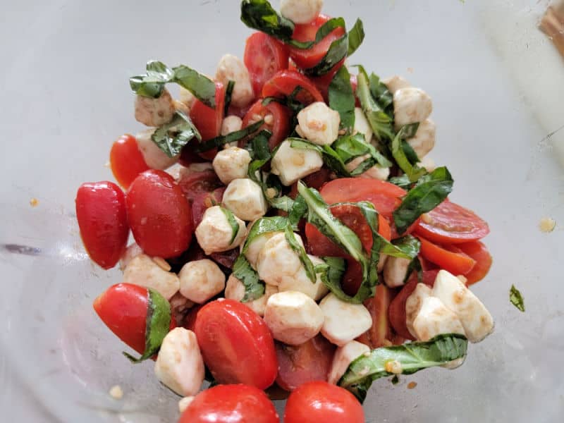 mozzarella balls, cut cherry tomatoes, basil strips in a glass bowl 