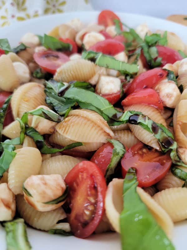 White bowl with pasta shells, cut chery tomatoes, and basil leaves in it. 