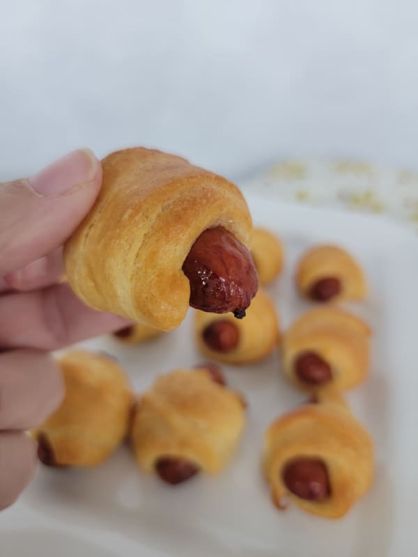 Hand holding a pigs in a blanket over a platter of them