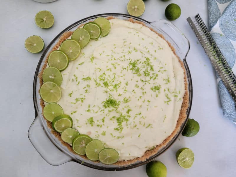 No bake key lime pie in a graham cracker crust in a glass pie dish next to a zester. 