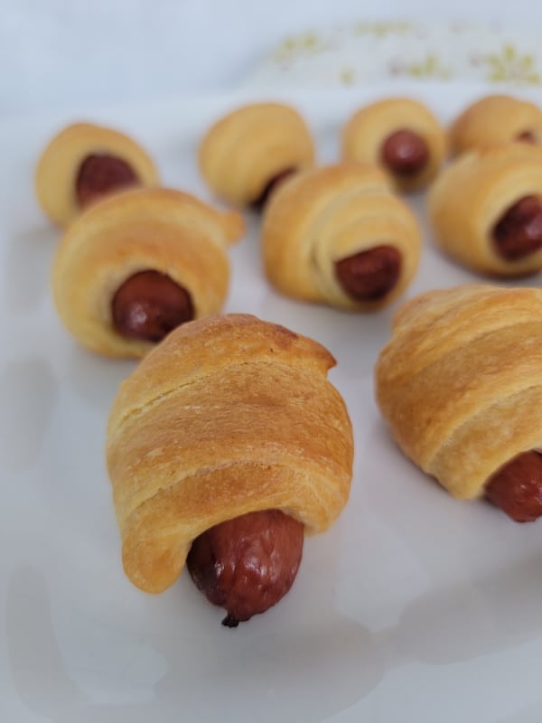 crescent dough wrapped around a sausage lined up on a white platter