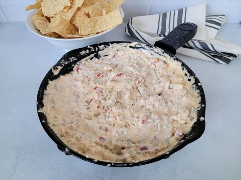 Velveeta dip in a cast iron skillet next to a white bowl of tortilla chips and a cloth napkin 