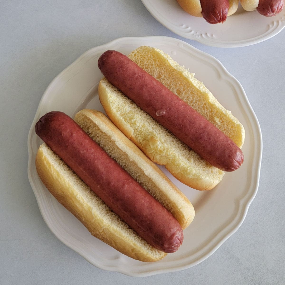 two hot dogs on buns places on a white plate