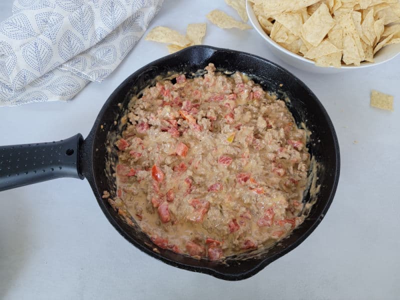 Rotel ground beef dip in a cast iron skillet next to a white bowl with tortilla chips and a cloth napkin