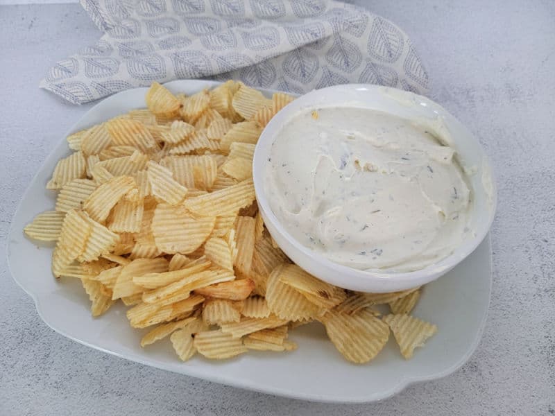 White plate with potato chips and a bowl of potato chip dip next to a cloth napkin 