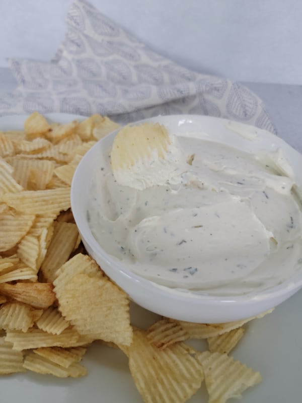 potato chip dipping into dip in a white bowl sitting on a white plate filled with potato chips