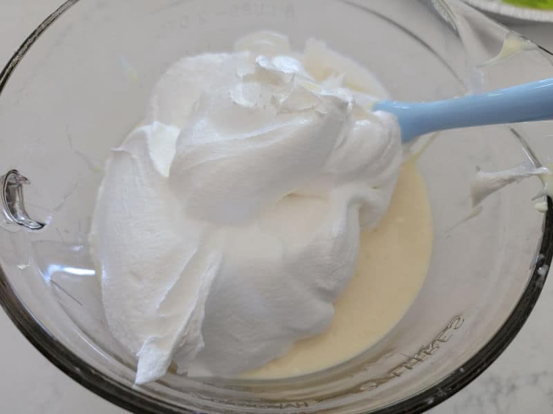 Cool whip on lemon pie mix in a glass bowl with a spatula 