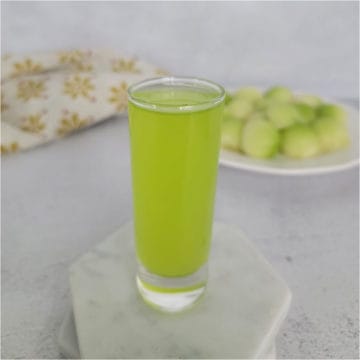 Melon Ball Shot on a white coaster next to a plate of melon