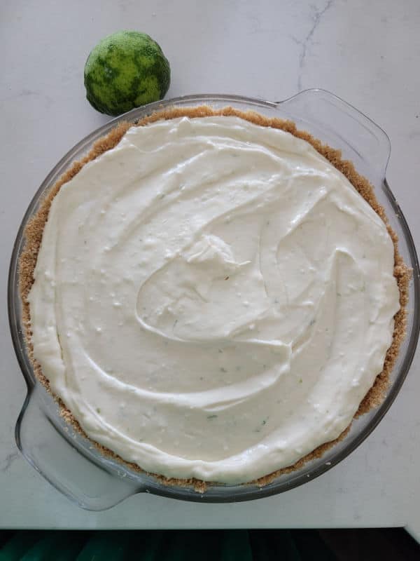 key lime pie in a graham cracker shell in a glass pie plate next to a lime
