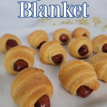 Pigs in a Blanket text over a white platter with smoked sausages wrapped in dough