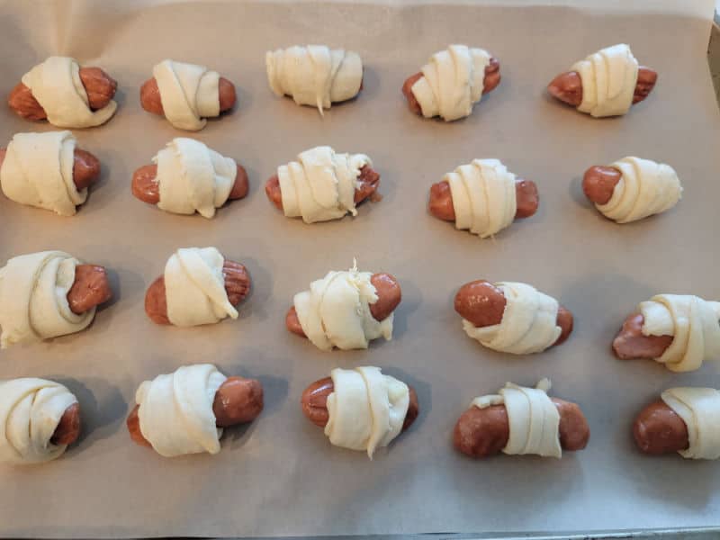 unbaked pigs in a blanket lined up on a parchment lined baking sheet