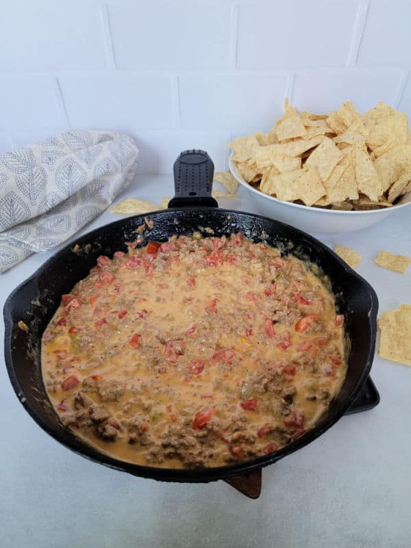 Rotel dip in a cast iron skillet next to a bowl of tortilla chips and a cloth napkin 