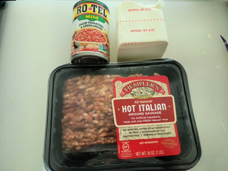 Can of Rotel diced tomatoes and green chilies, cream cheese, and hot Italian ground sausage on cutting board. 