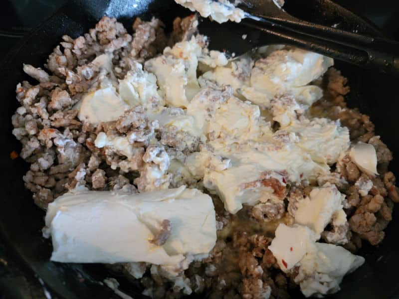 Cream cheese mixing into ground sausage in a cast iron skillet 