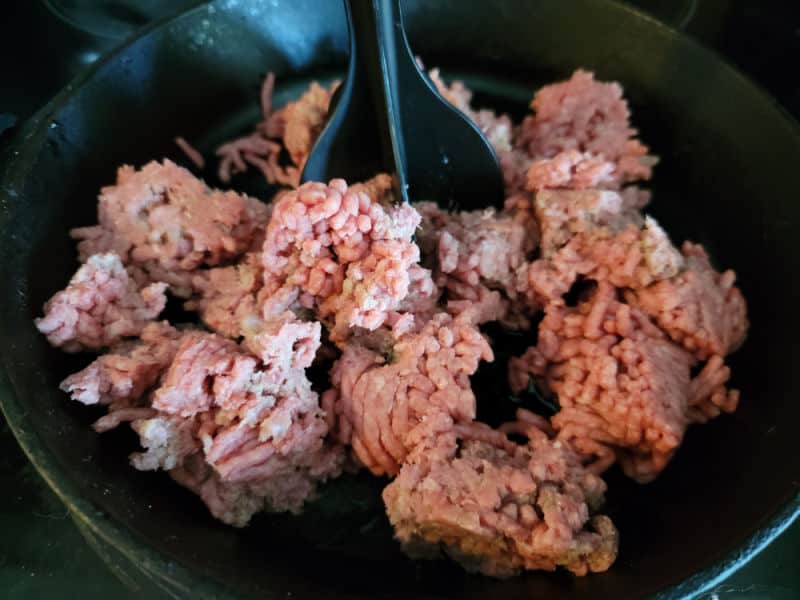 Ground beef being broken up in a cast iron skillet 