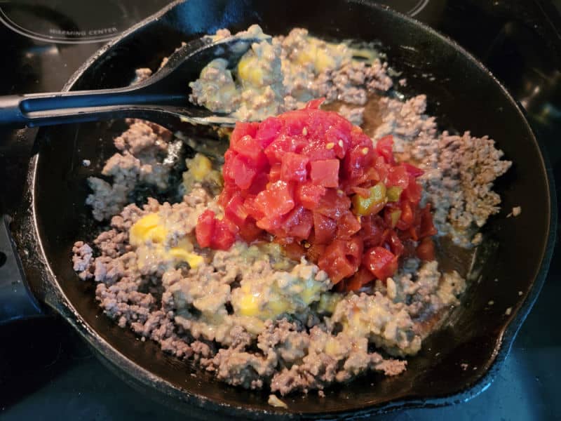 Diced tomatoes on top of velveeta and ground beef in a cast iron skillet 