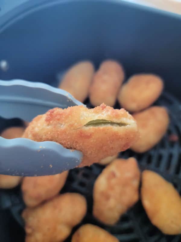 air fried jalapeno poppers held by tongs over the air fryer basket