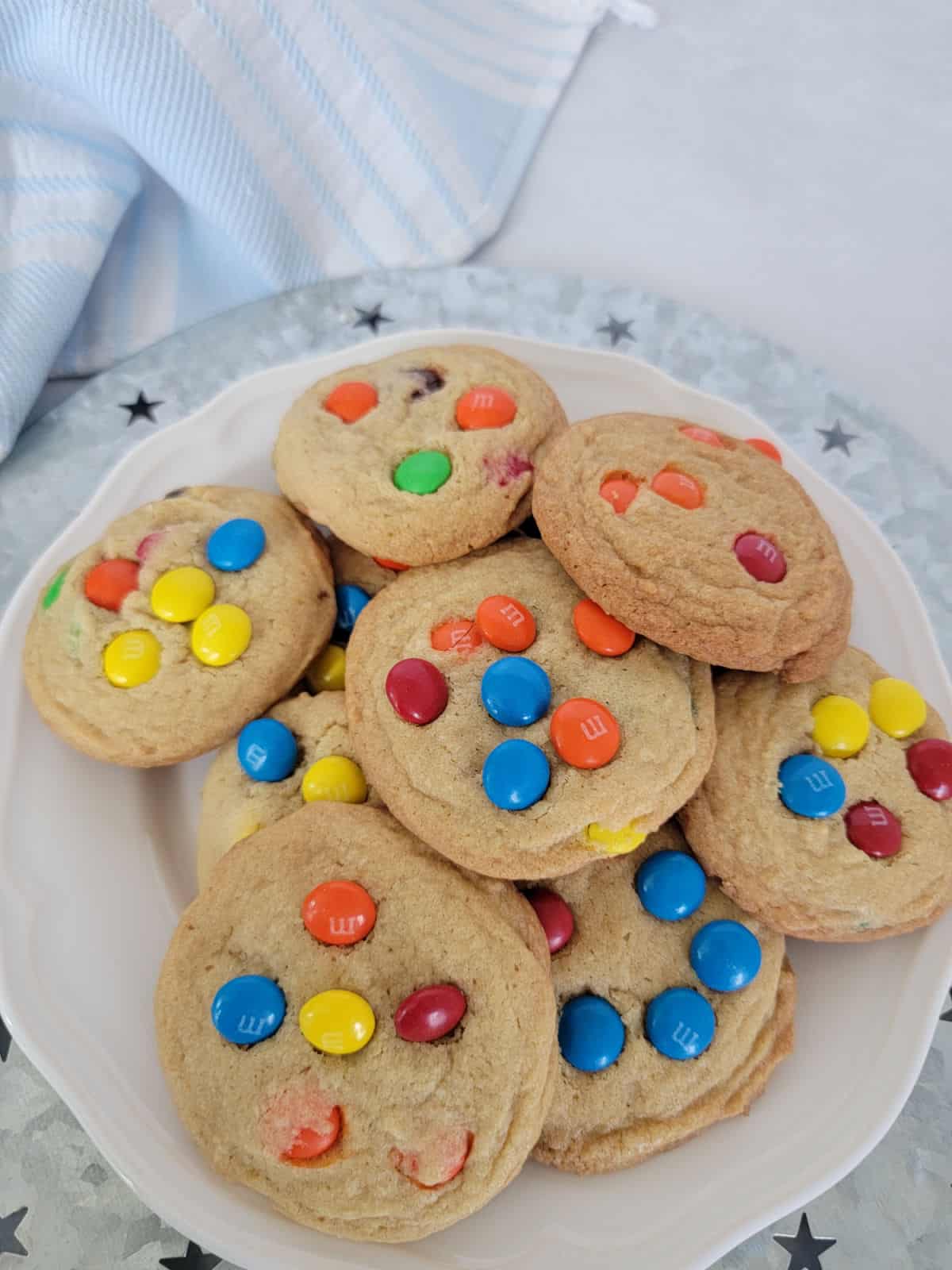 M&M Cookies on a white plate on a silver platter next to a cloth napkin