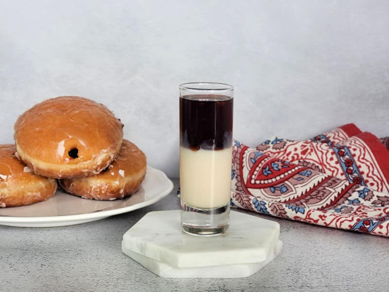 layered shot on white coasters next to a plate of jelly donuts and a cloth napkin 