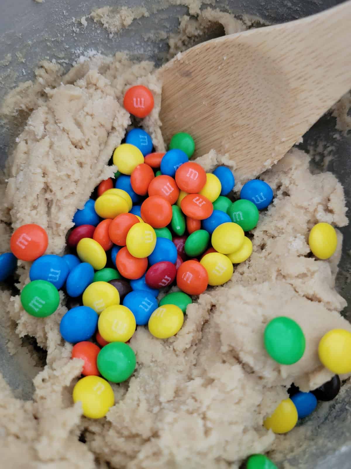 M&Ms in cookie dough with a wooden spoon