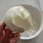 cupcake covered in icing being held over a bowl of coconut