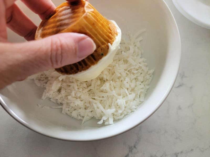 hand dipping a cupcake into a bowl of coconut