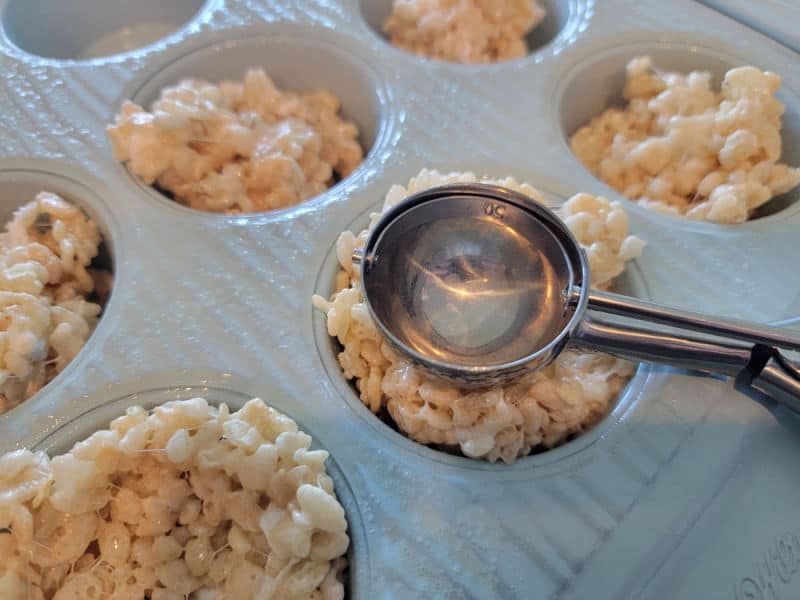 Cookie scoop pushing rice krispie treats into a muffin tin