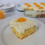 Square of pig pickin cake on a white plate in front of the baking dish and a stack of plates