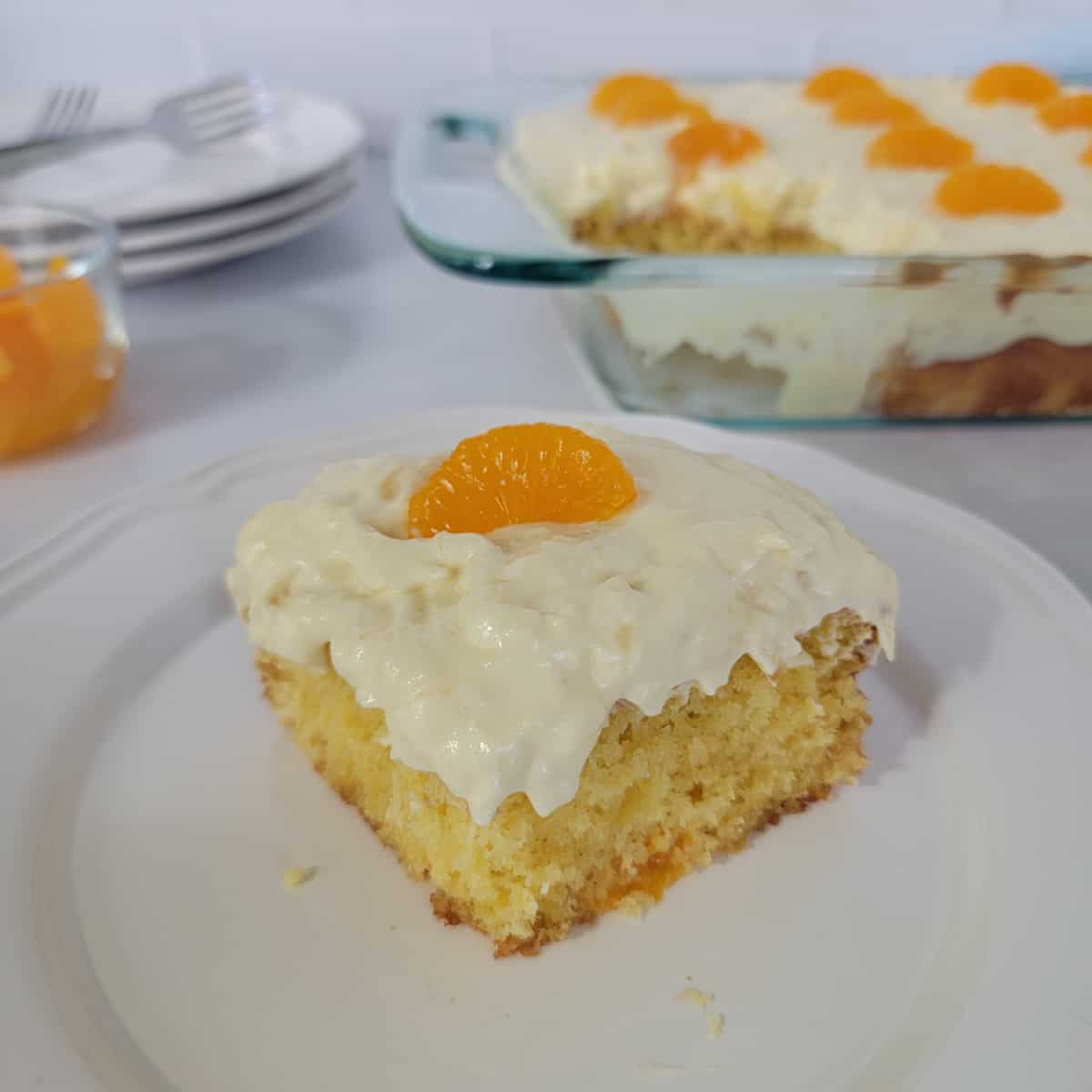 Square of pig pickin cake on a white plate in front of the baking dish and a stack of plates