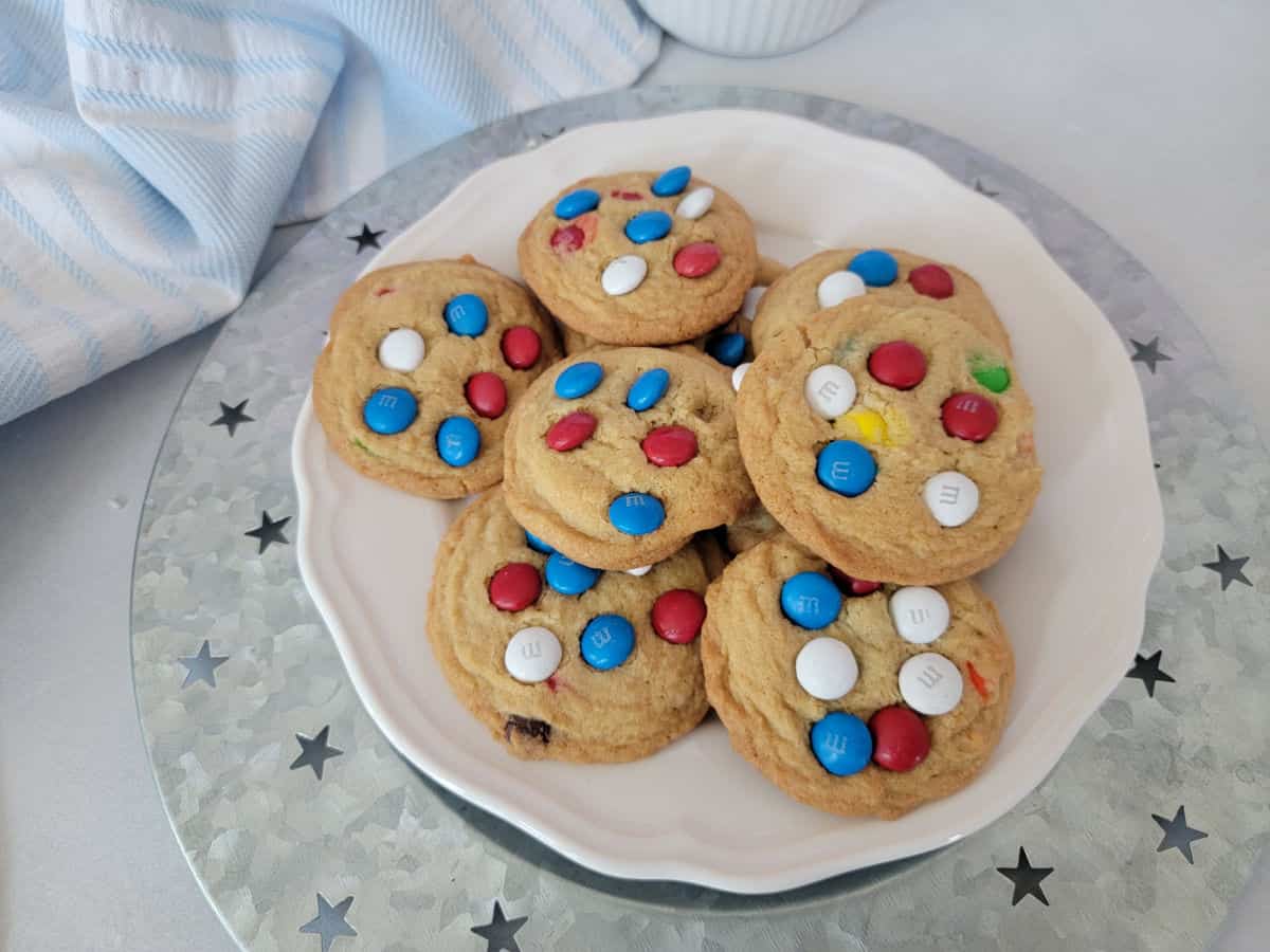 Red White and Blue M&M cookies on a white plate on a silver platter next to a cloth napkin
