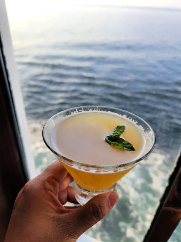Hand holding a spicy chipotle pineapple martini with the ocean in the background 