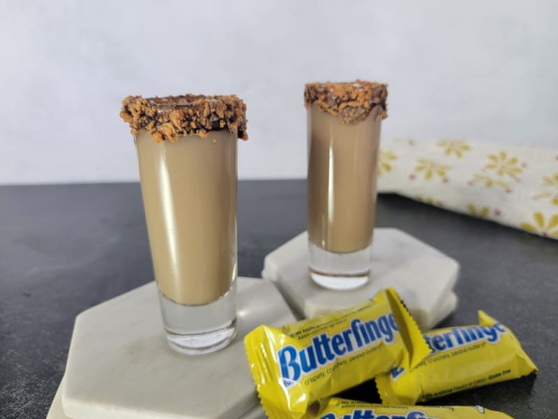 Two Butterfinger Shots on white coasters next to mini Butterfinger Chocolate bars