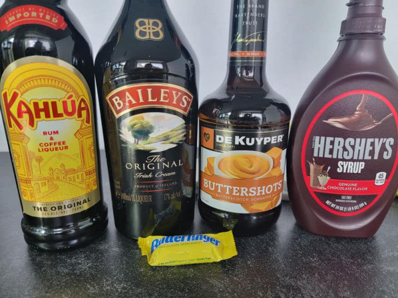 Kahlua, Baileys, Buttershot Liqueur, and Hersey Syrup bottles next to a small Butterfinger bar