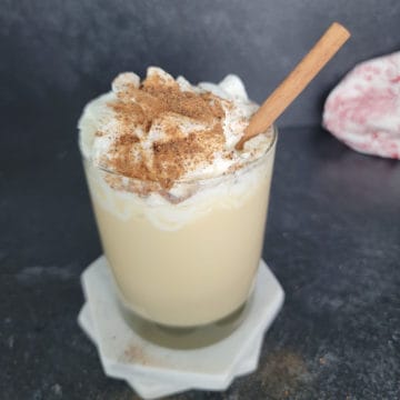 Eggnog Mudslide in a glass on a white coaster garnished with whipped cream and nutmeg with a cinnamon stick