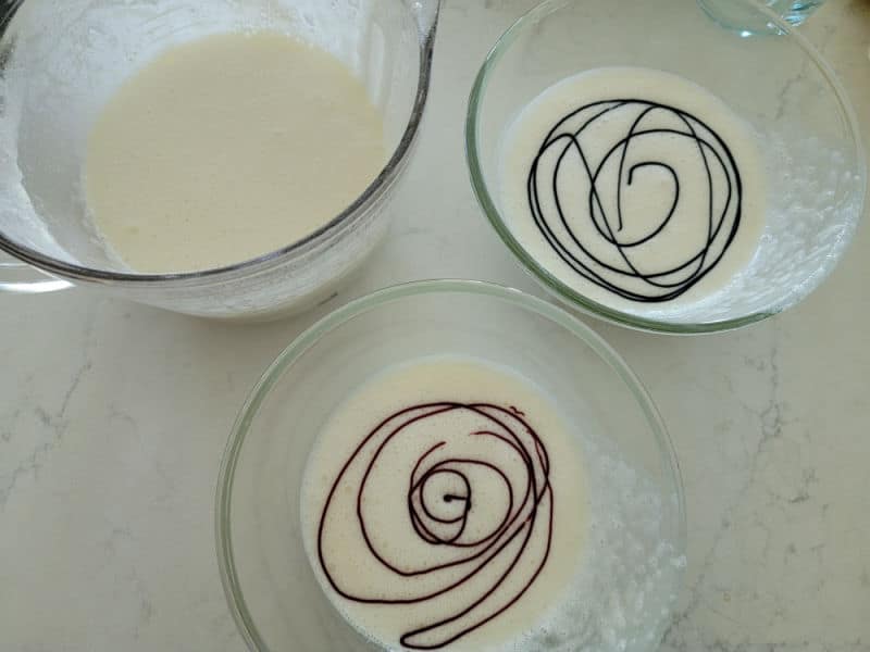Three glass bowls with cake batter, two of the bowls have swirls of color in them. 