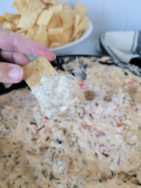 hand dipping a tortilla chip into Velveeta dip next to a bowl of tortilla chips 