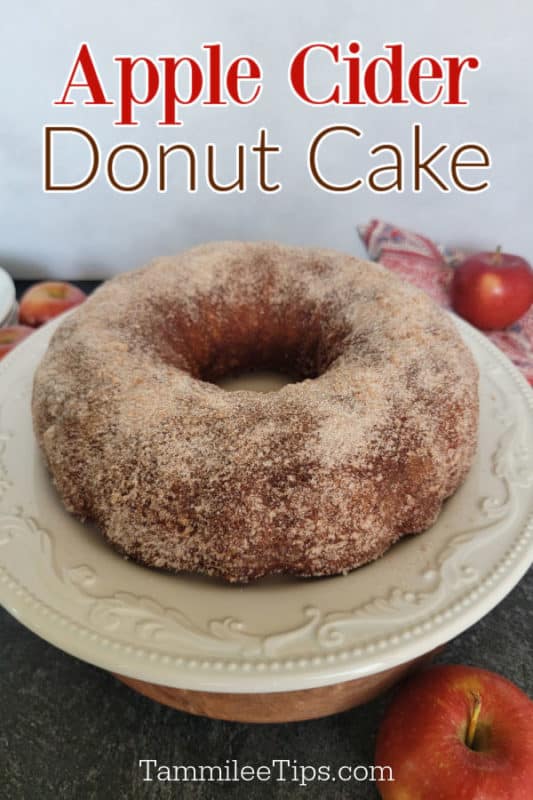 Apple Cider Donut Cake over a Bundt cake on a white cake plate next to apples