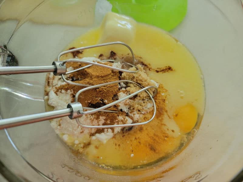 mixer beaters in a glass bowl with wet and dry cake ingredients