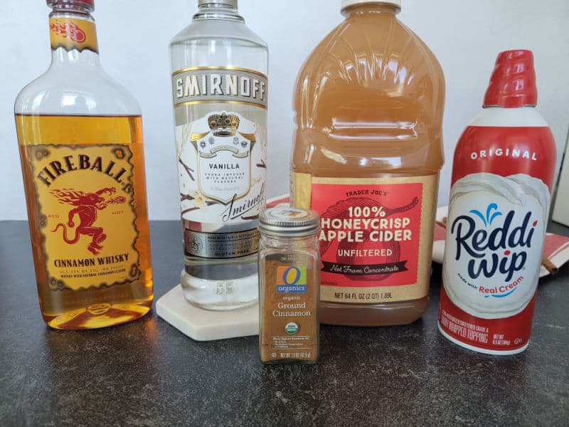 Fireball cinnamon whiskey, vanilla vodka, ground cinnamon, apple cider, and whipped cream can on a counter