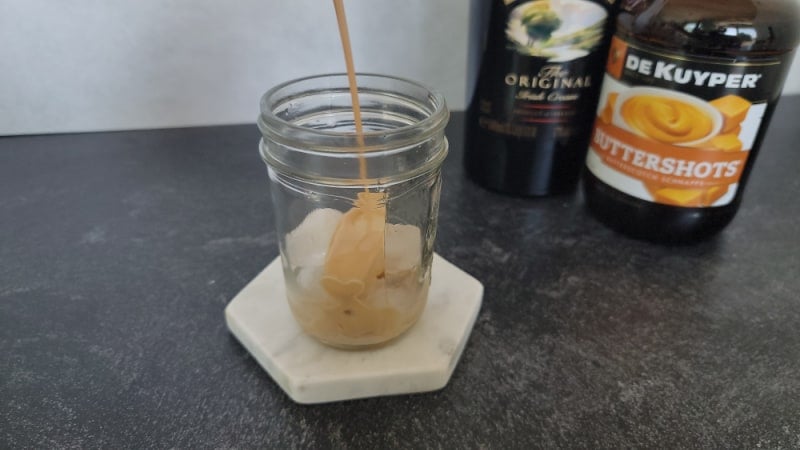 Irish cream pouring into a mason jar sitting on a marble coaster