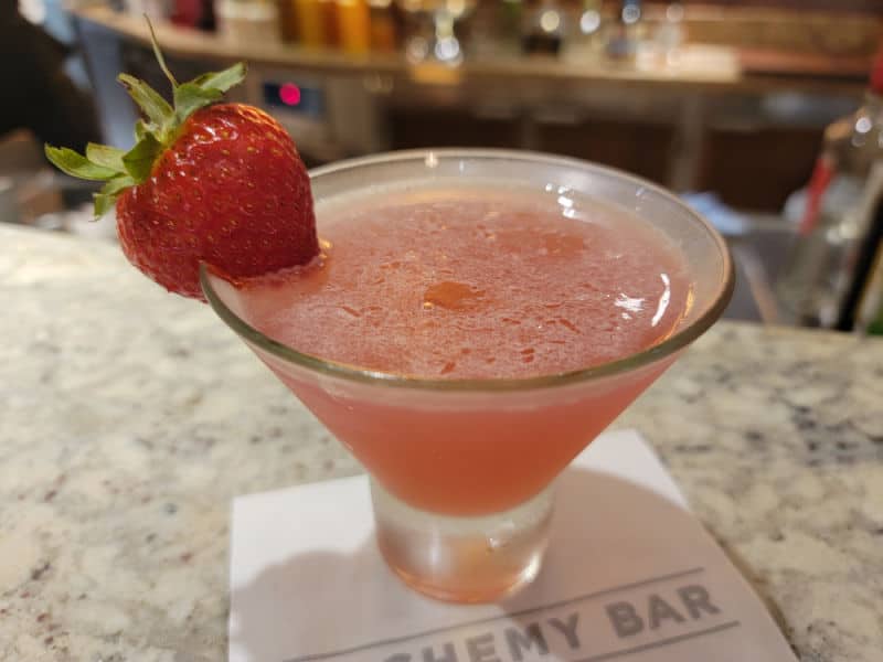 Curative Peach Cosmopolitan in a stemless martini glass on a white napkin with a strawberry garnish